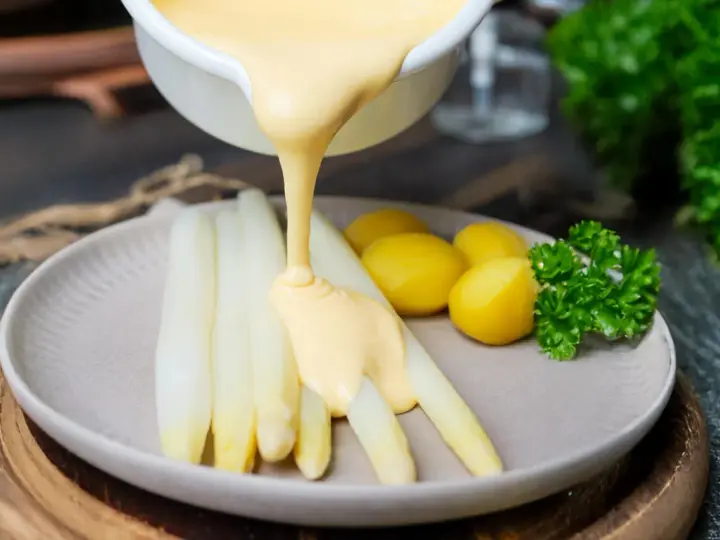 Sauce Hollandaise wird über weißen Spargel und Kartoffeln gegossen, um das Gericht zu verfeinern.