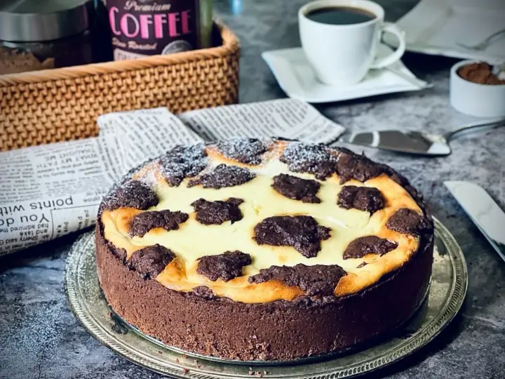 Ein köstlicher russischer Zupfkuchen mit Schokoladenboden und cremiger Füllung, bestäubt mit Puderzucker. Daneben eine Tasse Kaffee.