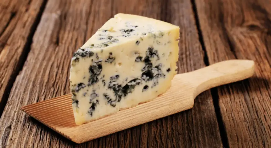 Ein Stück Blauschimmelkäse, perfekt für eine cremige blue cheese sauce, liegt auf einem Holzbrett.