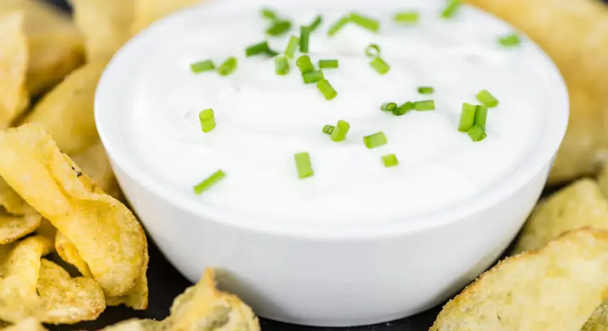 Schüssel mit cremiger Sour Cream, garniert mit Schnittlauch, umgeben von knusprigen Kartoffelchips.