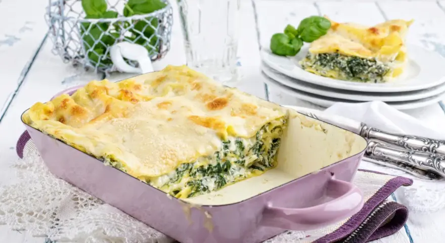 Herzhaftes Spinat-Lasagne-Rezept in einer lila Auflaufform, mit frischem Basilikum garniert.