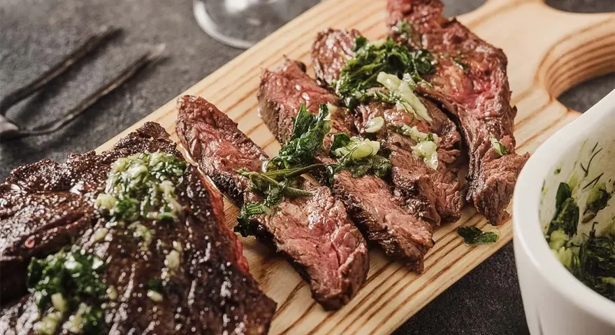 Saftiges, in Scheiben geschnittenes Flank Steak mit Kräutern und einer grünen Sauce auf einem Holzbrett serviert.