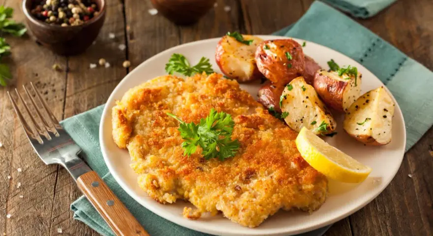 Goldbraunes Schnitzel, perfekt paniert, mit Rosmarinkartoffeln und Zitrone auf einem Teller. Ein Genuss, der zeigt, wie man ein Schnitzel paniert.
