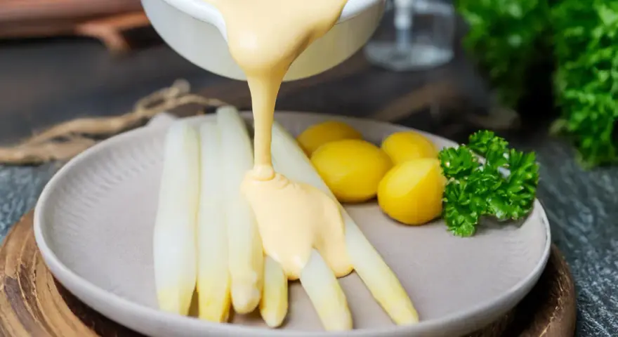 Sauce Hollandaise wird über weißen Spargel und Kartoffeln gegossen, um das Gericht zu verfeinern.