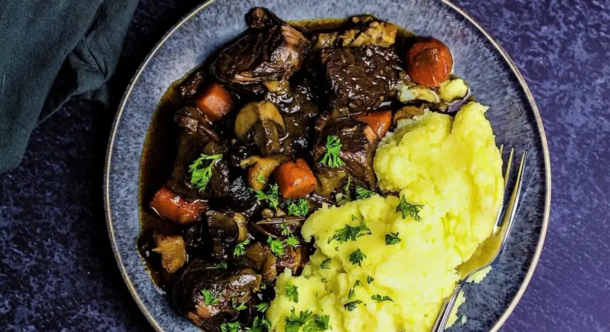 Herzhaftes Boeuf Bourguignon mit zartem Rindfleisch, Karotten und Pilzen, serviert mit cremigem Kartoffelpüree und Petersilie.