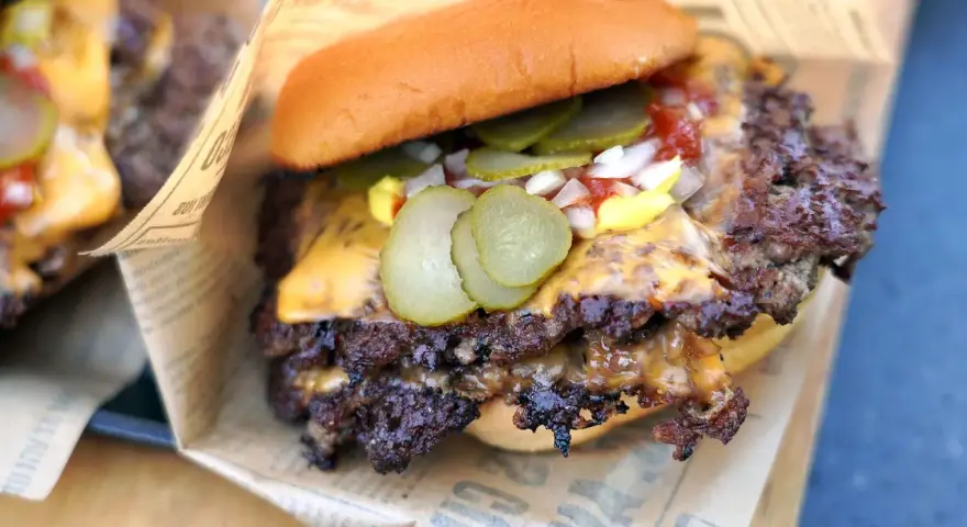 Saftiger Smash Burger mit geschmolzenem Käse, Gurken, Zwiebeln und Ketchup auf einem Brötchen, eingewickelt in Papier.