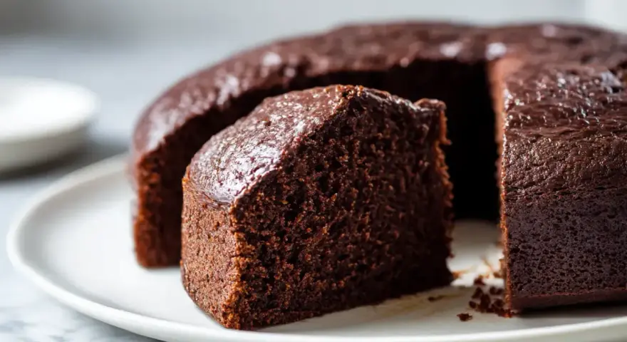 Saftiger Schokoladenkuchen, frisch aus dem Airfryer, auf einer weißen Platte. Ein Stück ist bereits angeschnitten.