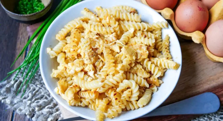 Fusilli-Nudeln mit Rührei, gewürzt mit Pfeffer. Daneben liegen frische Eier und Schnittlauch. Ein einfaches, aber leckeres Gericht: Nudeln mit Ei.