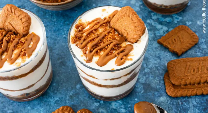 Schichtdessert im Glas: cremiges Lotus Cheesecake mit Keksbröseln und Karamellsoße, garniert mit einem Lotus Keks.