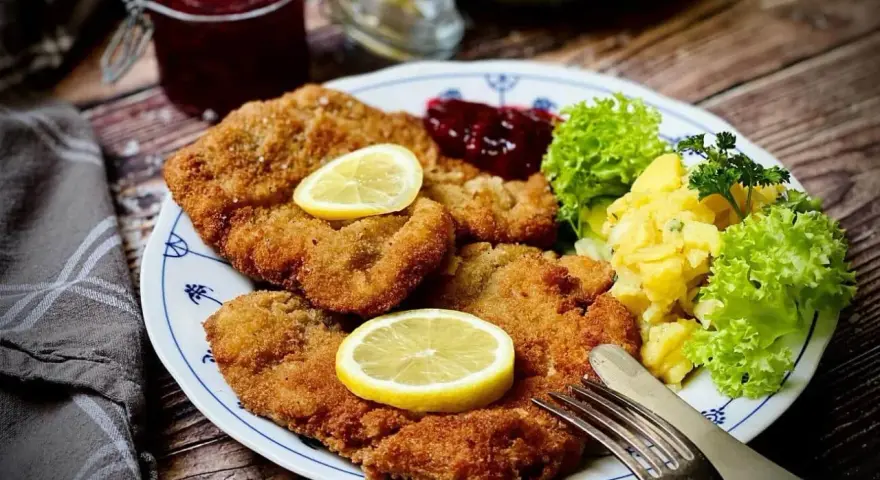 Ein köstlicher **Garnitur Wiener Schnitzel** mit Kartoffelsalat, Preiselbeeren und Zitrone auf einem Teller.
