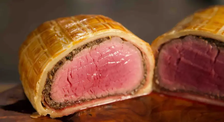 Ein perfekt zubereitetes Beef Wellington, saftig rosa im Inneren, umhüllt von goldbraunem Blätterteig.