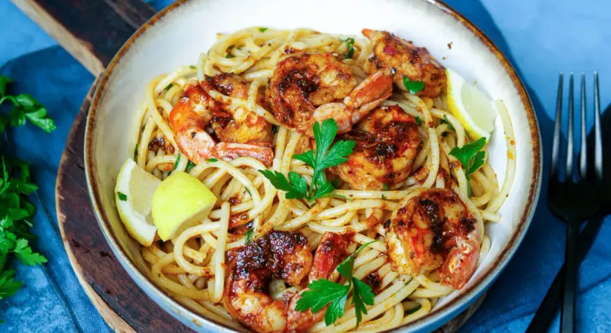 Ein Teller mit köstlichen Spaghetti mit Garnelen, garniert mit frischer Petersilie und Zitronenspalten.