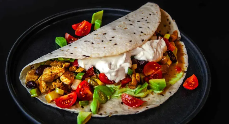 Saftige Fajitas de pollo mit Hähnchen, Gemüse, Avocado und einem Klecks Sauerrahm auf einem Tortilla-Wrap.