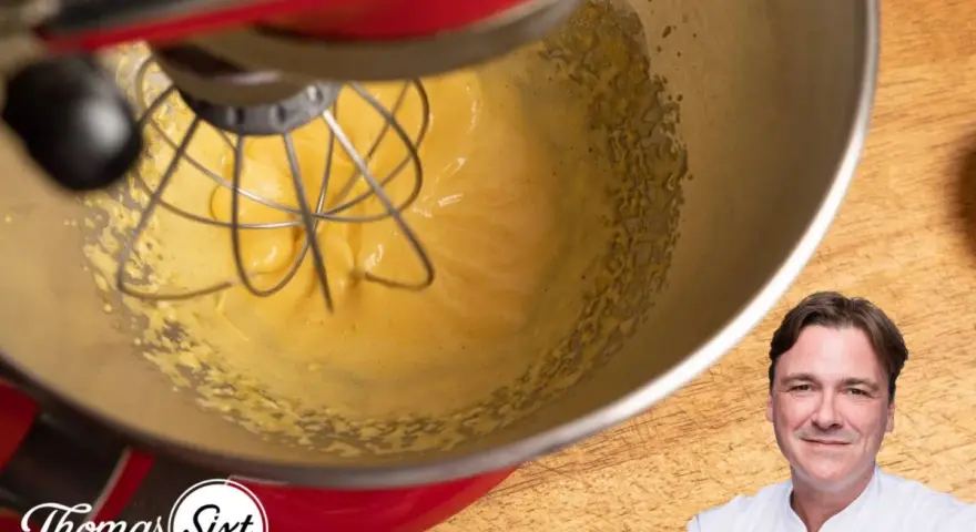 Küchenmaschine mixt eine cremige, gelbe Masse, die an Sauce Hollandaise erinnert. Ein Koch lächelt im Vordergrund.