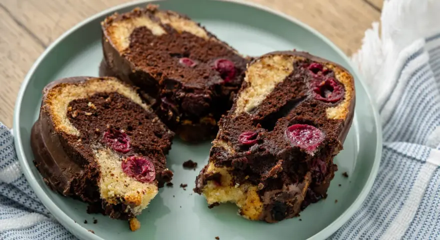 Drei saftige Stücke Marmorkuchen mit Kirschen und Schokoladenglasur auf einem Teller.