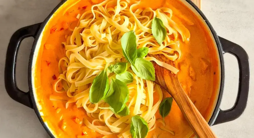 Cremiges Chicken Alfredo mit Tagliatelle, garniert mit frischem Basilikum, in einer schwarzen Pfanne.