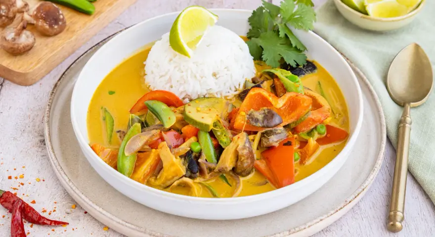 Ein bunter Thai Curry ohne Kokosmilch mit Reis, Paprika, Zucchini und Pilzen, garniert mit Limette und Koriander.