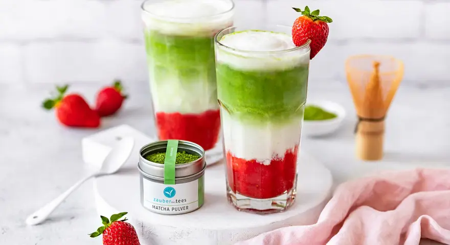 Zwei geschichtete Erdbeer-Matcha-Latte-Getränke mit frischen Erdbeeren und Matcha-Pulver.