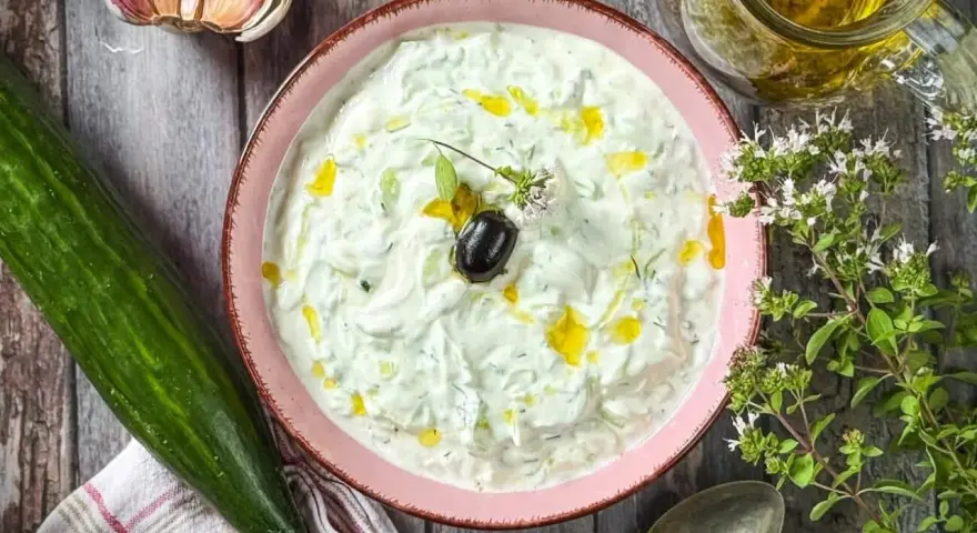 Frischer Tzatziki selbst machen: Cremiger Joghurt mit Gurke, Knoblauch, Dill und Olivenöl. Dazu eine Olive und Kräuter.