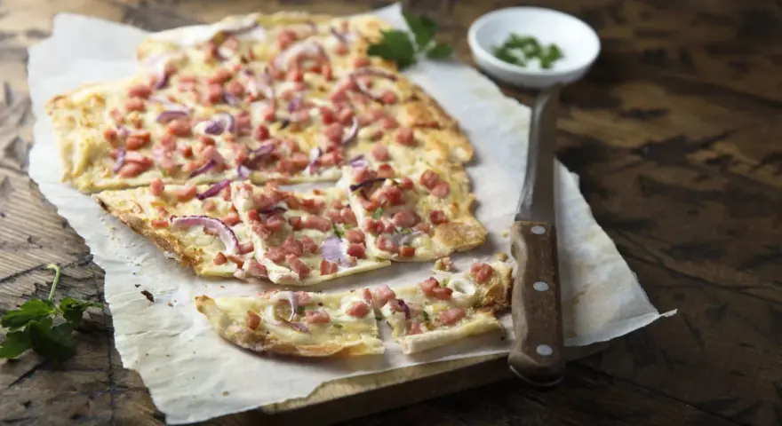 Flammkuchen mit Speck und Zwiebeln, eine klassische Idee für Flammkuchen Belag. Frisch und knusprig auf Holz serviert.