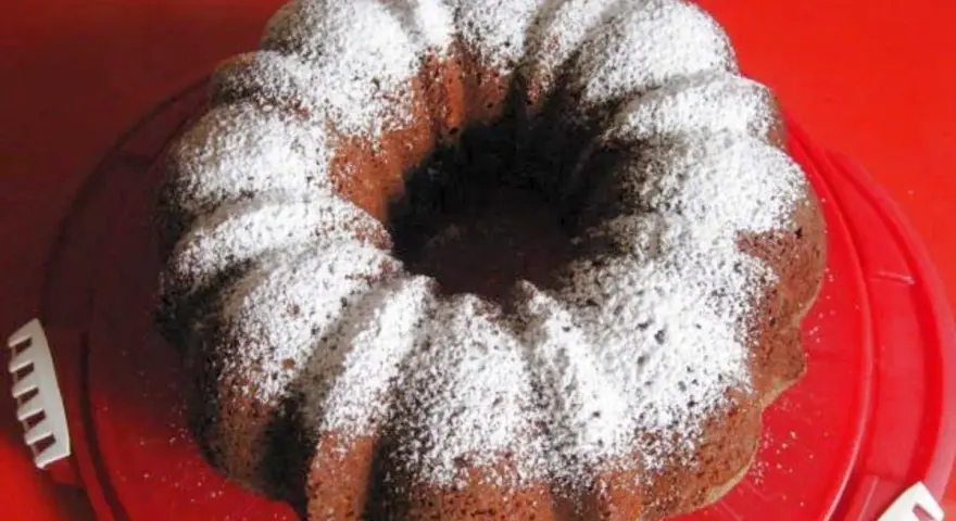 Omas Nusskuchen Gugelhupf, mit Puderzucker bestäubt, auf einem roten Teller.