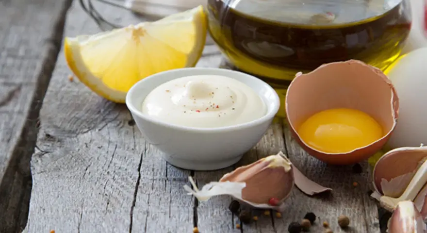 Cremige Mayonnaise mit gekochtem Eigelb und Joghurt, garniert mit Pfeffer, neben Zitrone, Knoblauch und Olivenöl.
