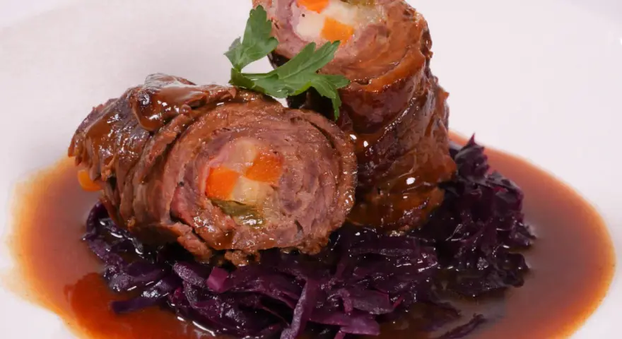 Zwei Rouladen mit Gemüsefüllung, serviert mit Rotkohl und Bratensoße. Köstliche Rouladen im Backofen zubereitet.