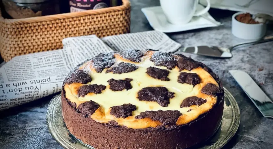 Ein köstlicher russischer Zupfkuchen mit Schokoladenboden und cremiger Füllung, bestäubt mit Puderzucker. Daneben eine Tasse Kaffee.
