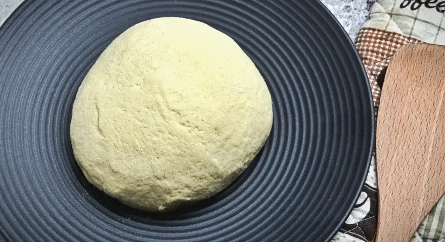 Ein runder Pizzateig auf schwarzer Platte wartet darauf, zu wissen, wie lange muss ein pizzateig ruhen, bevor er perfekt wird.