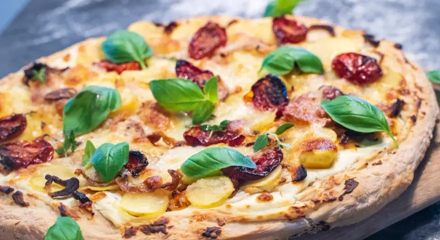 Eine köstliche Pizza Bianca mit Kartoffelscheiben, getrockneten Tomaten und frischem Basilikum.