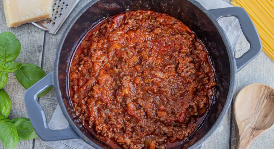 Herzhaftes Bolognese-Rezept original in einem Topf, mit frischem Basilikum, Parmesan und Spaghetti daneben.