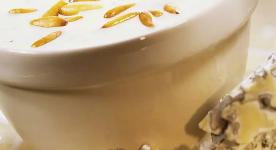 Cremige Gorgonzola-Sauce mit gerösteten Pinienkernen in einer Schüssel, daneben ein Stück Gorgonzola.