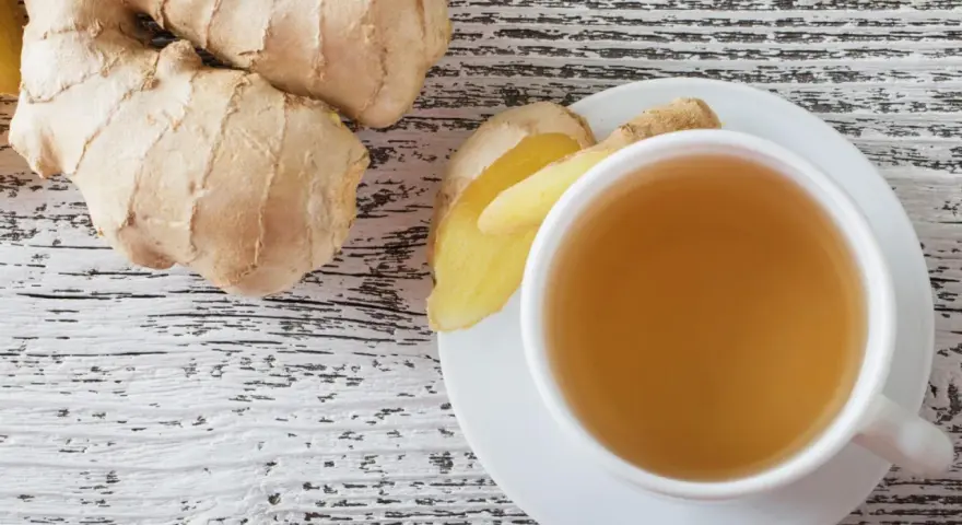 Frischer Ingwer und eine Tasse Ingwertee auf Holzhintergrund. Vielleicht ein kleiner Fehler bei der Zubereitung, wenn der Tee zu stark ist.