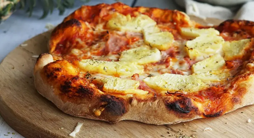 Eine köstliche Pizza Hawaii mit saftigen Ananasstücken und Schinken auf knusprigem Teig, garniert mit Kräutern.