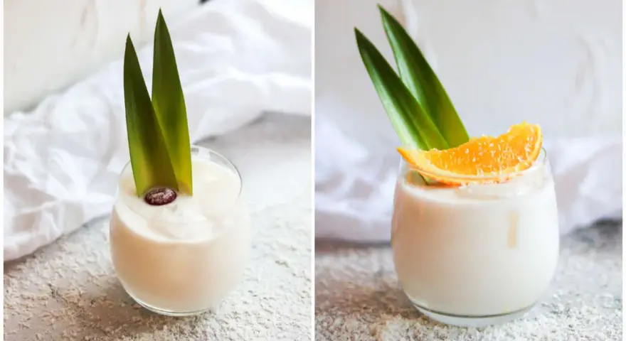 Zwei Gläser cremiger, alkoholfreier Piña Colada, garniert mit Ananasblättern und einer Orangenscheibe bzw. einer Beere.