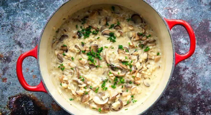 Cremiges Pilzrisotto in rotem Topf, garniert mit Schnittlauch.