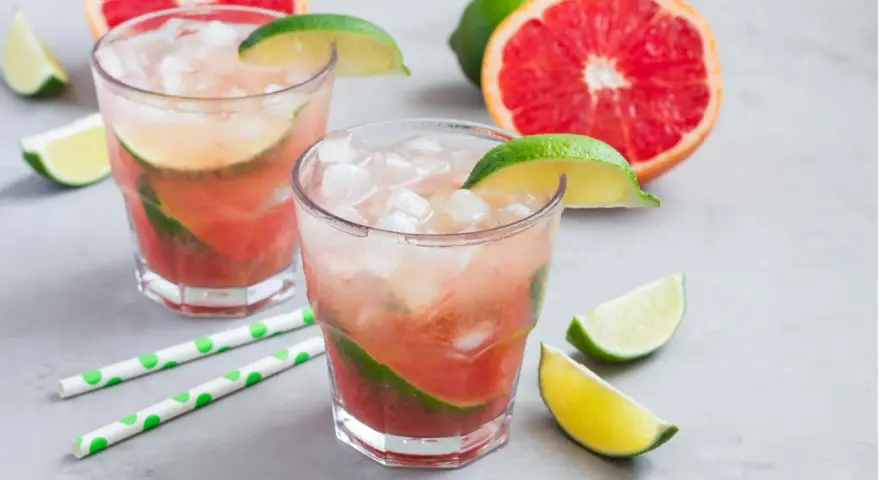 Erfrischender Aperol Paloma mit Grapefruit und Limette, serviert mit Eis und grünen Trinkhalmen.