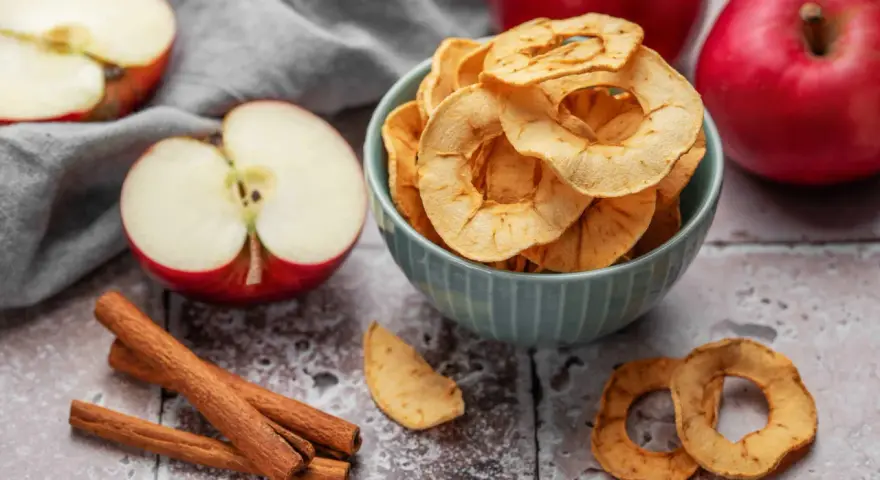 Leckere Apfelchips, die man ganz einfach selber machen kann, in einer Schüssel mit frischen Äpfeln und Zimtstangen.
