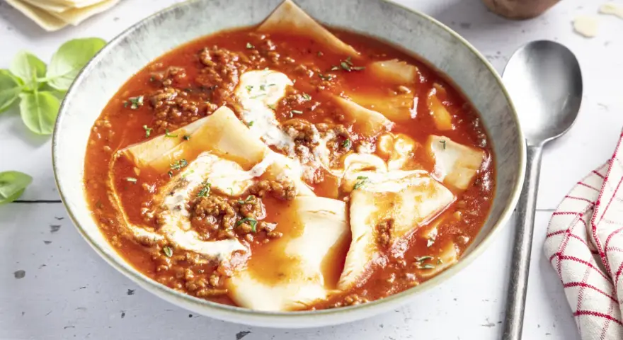 Herzhafte Lasagne Suppe in einer Schüssel, mit Hackfleischsauce, Nudelplatten und einem Klecks Sahne. Frisch garniert mit Basilikum.