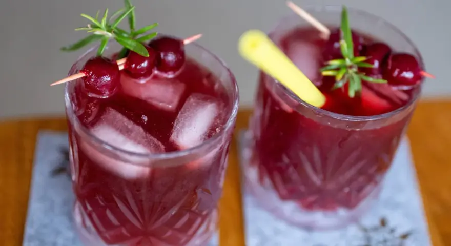 Zwei erfrischende, rote Mocktails mit Kirschen und Rosmarin, perfekt für einen entspannten Abend.