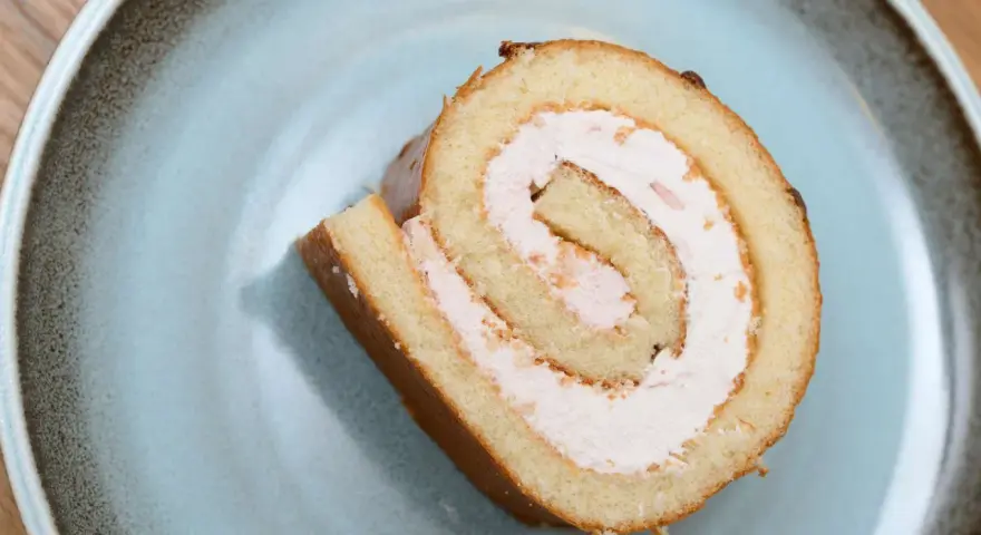 Ein Stück Biskuitrolle mit 5 Eiern und rosa Füllung auf einem blauen Teller.