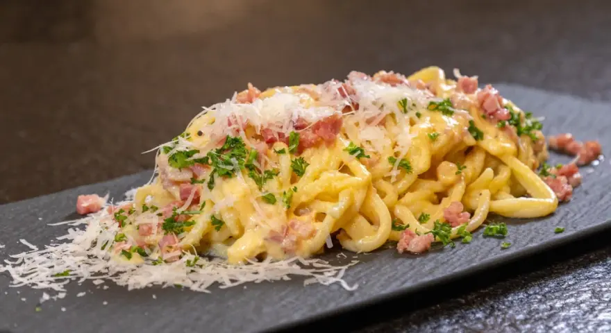 Ein Teller cremiger Spaghetti Carbonara, garniert mit Speckwürfeln, Petersilie und frisch geriebenem Parmesan.