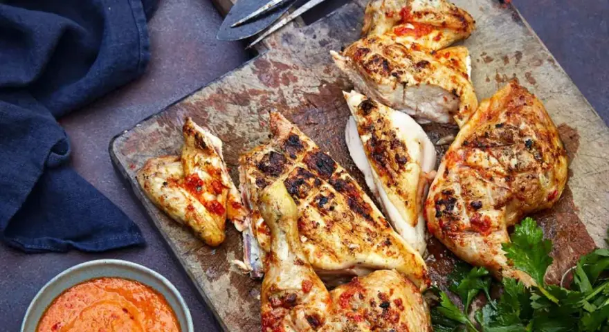 Saftiges Peri Peri Chicken, gegrillt und mit einer würzigen Sauce serviert, liegt auf einem Holzbrett.