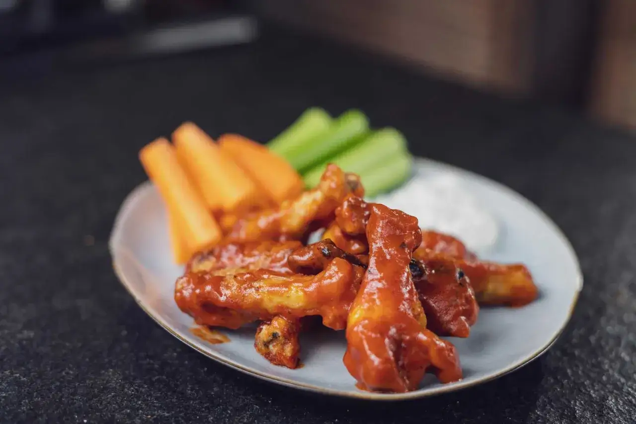 Saftige Chicken Wings in scharfer Marinade, serviert mit Karotten- und Selleriesticks sowie Dip.