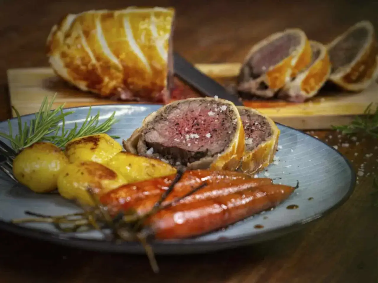 Ein perfekt zubereitetes Beef Wellington mit zarten Kartoffeln und glasierten Karotten, garniert mit Rosmarin.