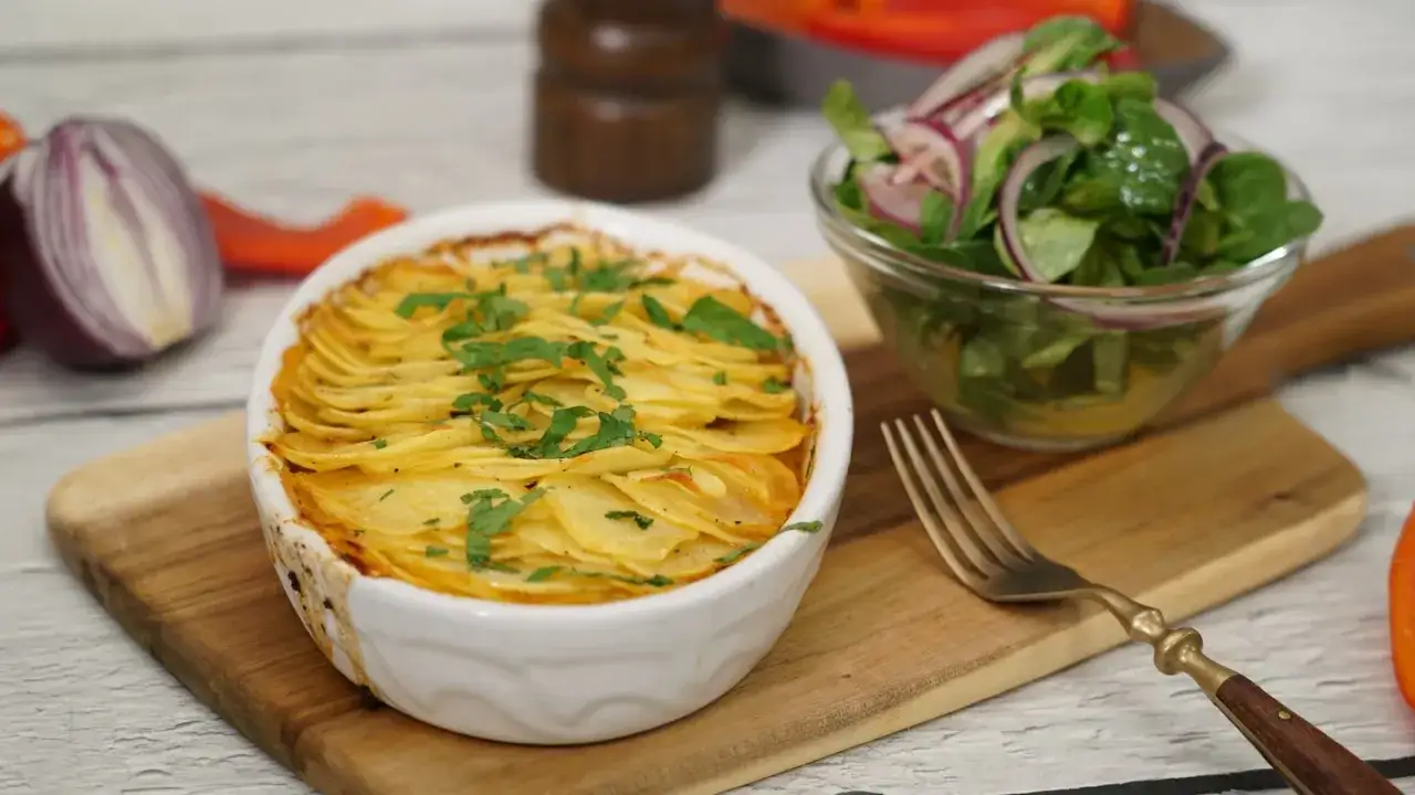 Herzhaftes Shepherd's Pie mit knuspriger Kartoffeldecke, garniert mit Petersilie, daneben ein frischer Salat mit roten Zwiebeln.