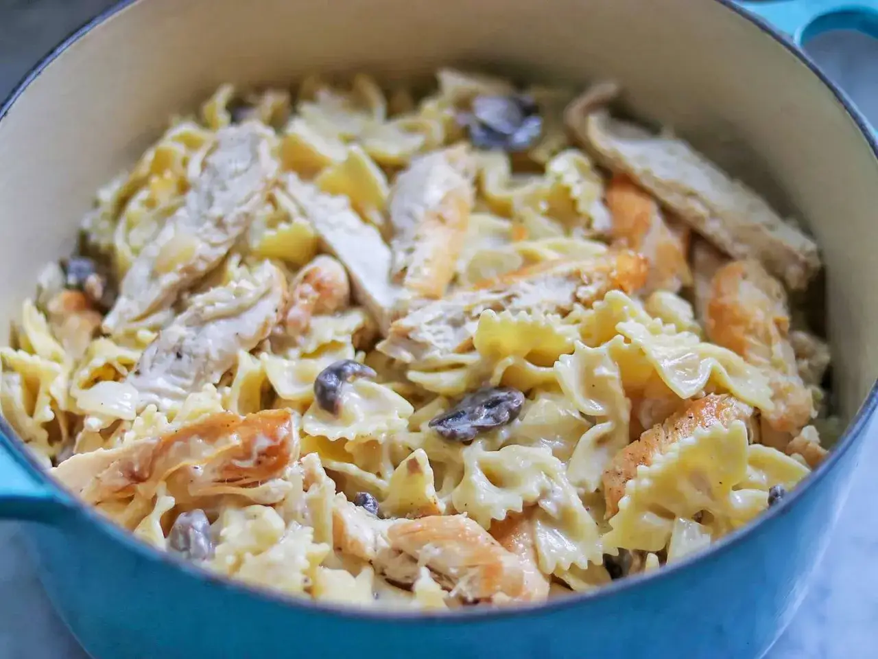 Herzhaftes Chicken Alfredo mit Farfalle-Nudeln und Pilzen in einer cremigen Sauce, serviert in einem blauen Topf.