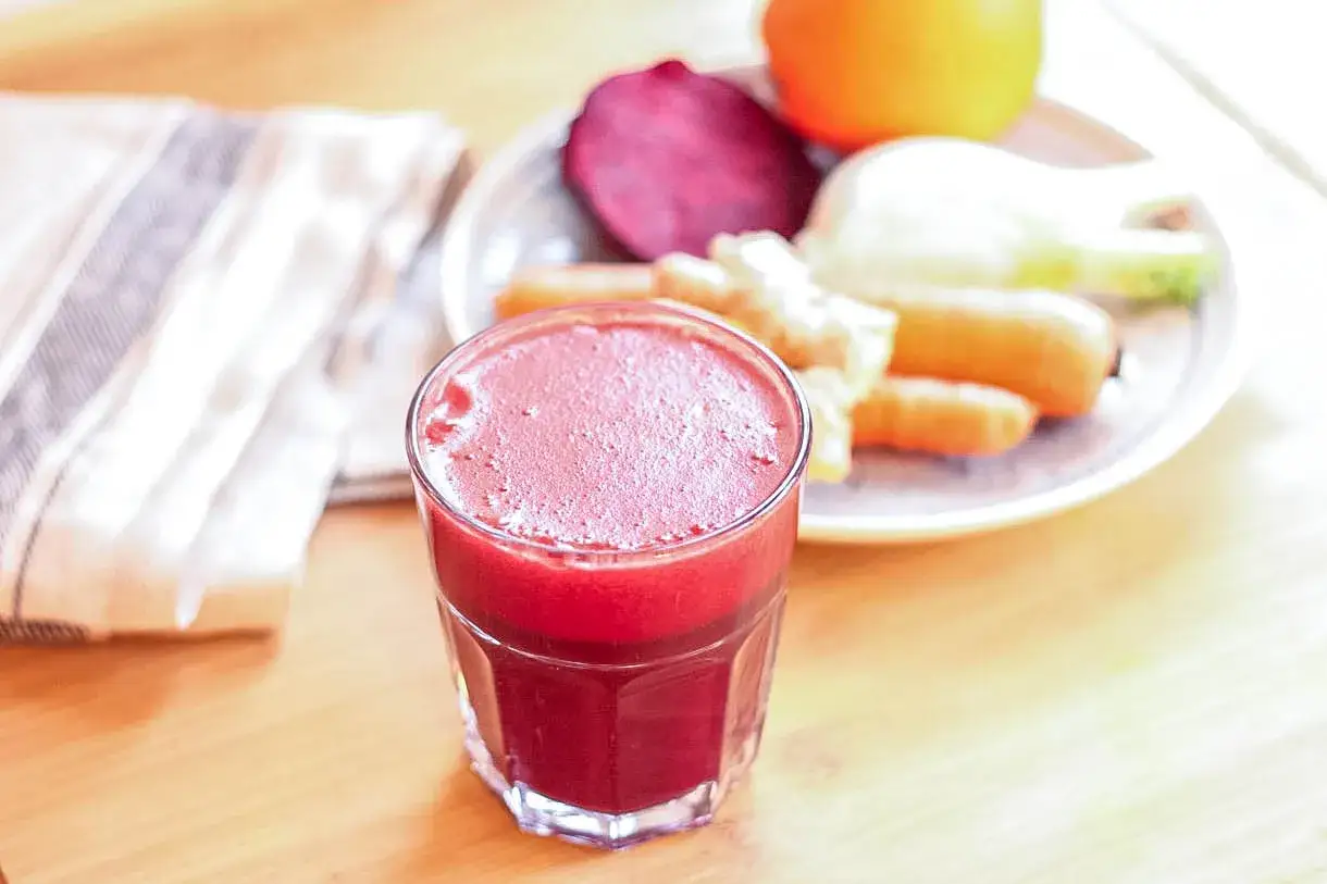 Frisch gepresster Rote-Bete-Saft, perfekt, um zu Hause saft selber machen. Daneben liegen Karotten, Rote Bete, Fenchel und eine Orange.