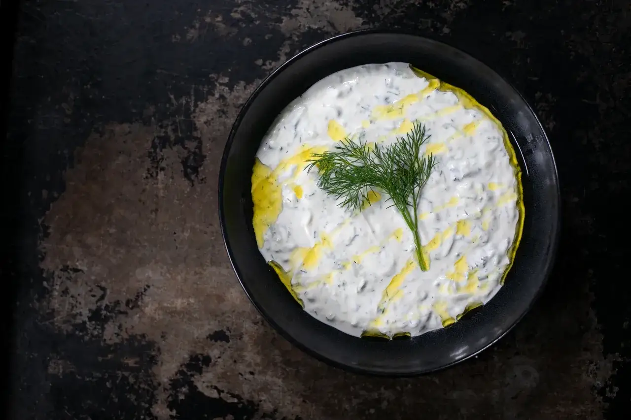 Frischer Tzatziki selbst machen: cremiger Joghurt mit Gurke, Dill und Oliven&ouml;l in einer schwarzen Sch&uuml;ssel.