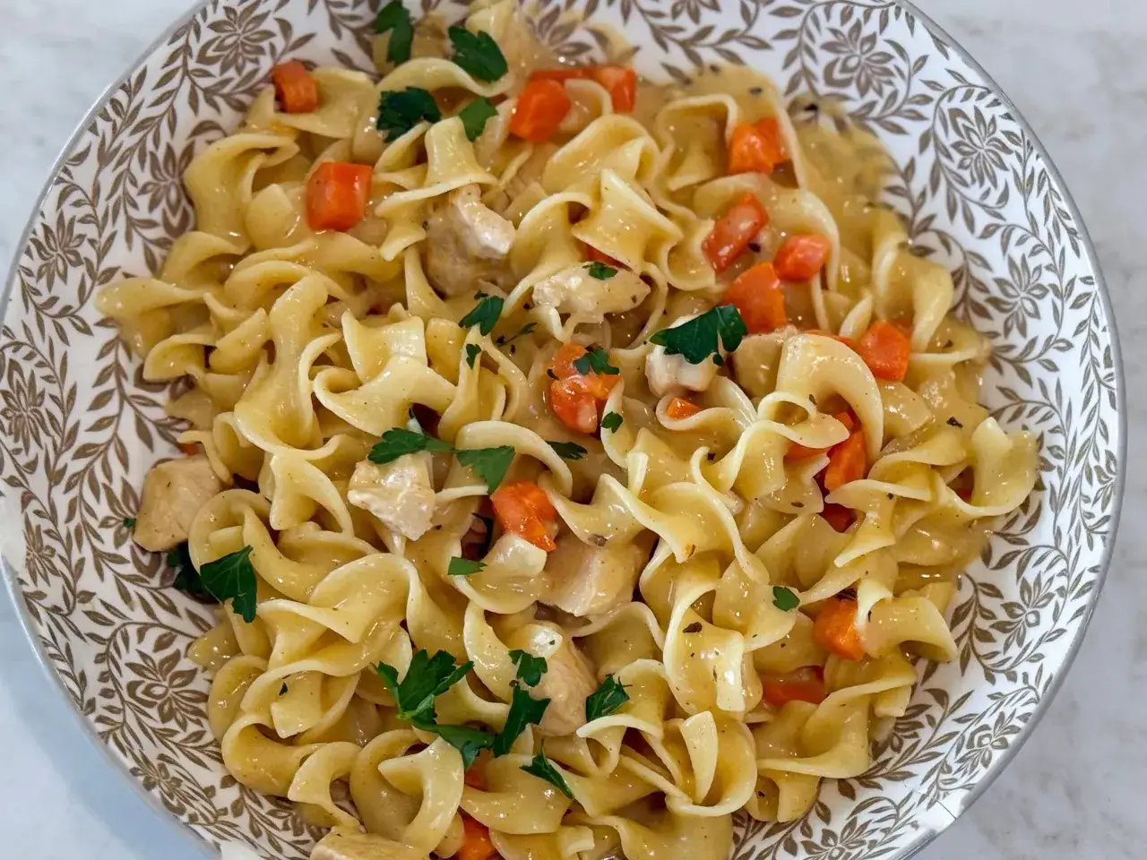 Herzhafte nudeln mit ei, Hühnchen und Karotten in einer cremigen Sauce, garniert mit Petersilie.